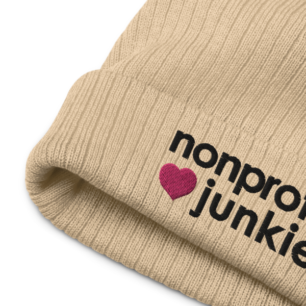 Beige ribbed knit beanie, black text on one side says nonprofit junkie in regular arial like font next to a pink heart