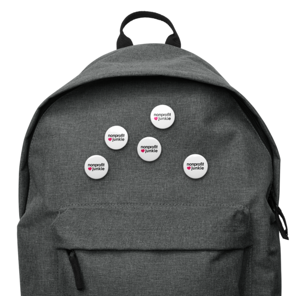 Set of white pin buttons, black text on one side says nonprofit junkie in regular arial like font next to a pink heart, on a backpack