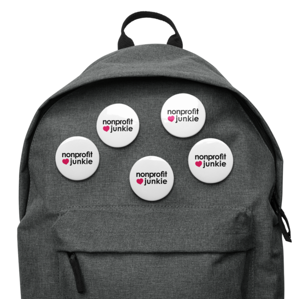 Set of white pin buttons, black text on one side says nonprofit junkie in regular arial like font next to a pink heart, on a backpack