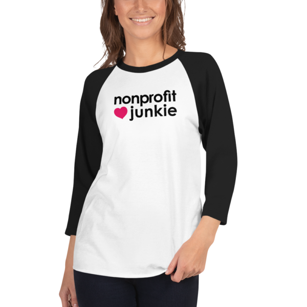 Black 3 4th sleeve raglan shirt, white in middle, black text on one side says nonprofit junkie next to a pink heart, on a woman