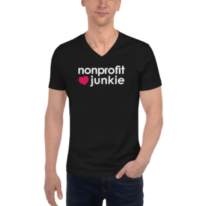 Unisex black v neck t shirt, white text on one side says nonprofit junkie in regular arial font next to a pink heart on a man