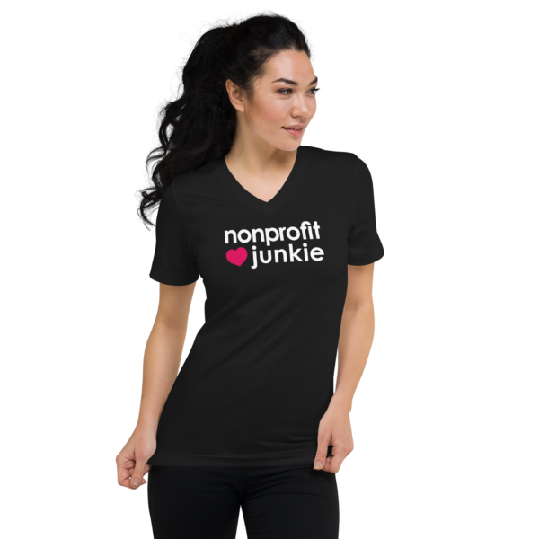 Unisex black v neck t shirt, white text on one side says nonprofit junkie in regular arial font next to a pink heart on a woman