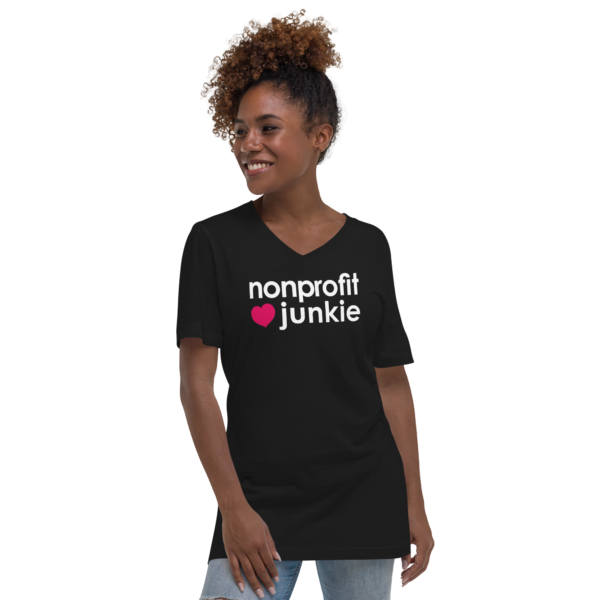 Unisex black v neck t shirt, white text on one side says nonprofit junkie in regular arial font next to a pink heart on a woman